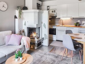 A modern living room with a fireplace, a sofa, a coffee table with plants, and a kitchen area with cabinets and a sink. - Rukaköngäs 21 by Interhome (Kuusamo)