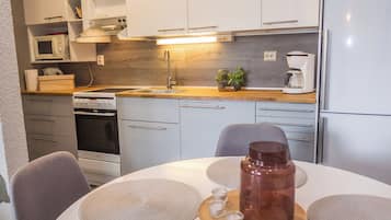 A modern kitchen with white cabinetry, a built-in oven, a coffee maker, and a dining table with placemats and a glass pitcher.