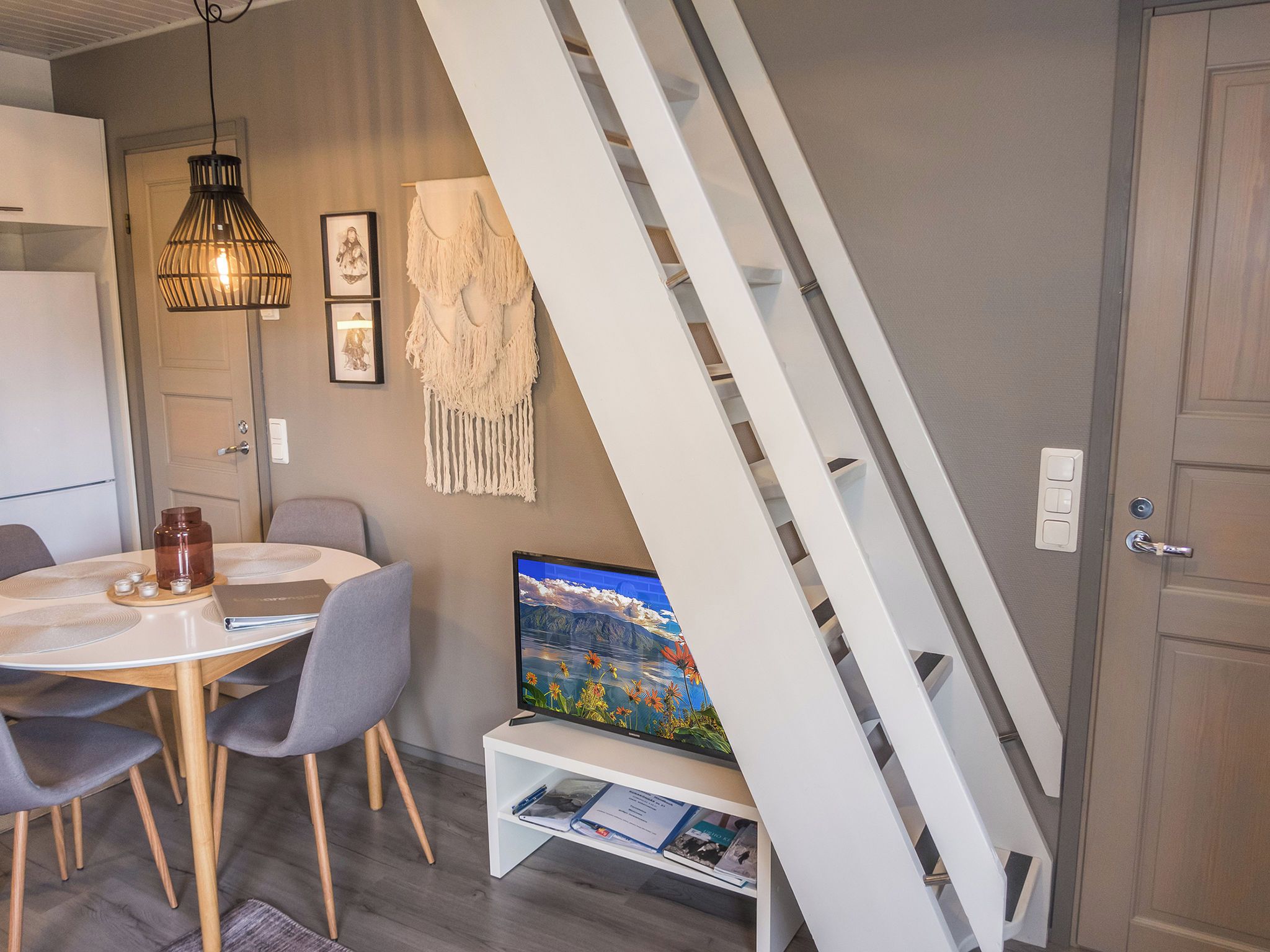 A modern dining area with a round table, chairs, a television, and a staircase.