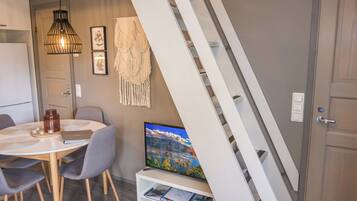 A modern dining area with a round table, chairs, a television, and a staircase.