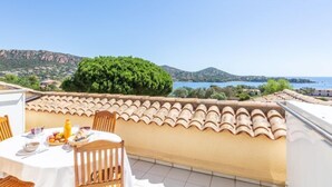 Eine Terrasse mit Esstisch, mit Blick auf eine Küstenlandschaft mit Hügeln und einem Gewässer.