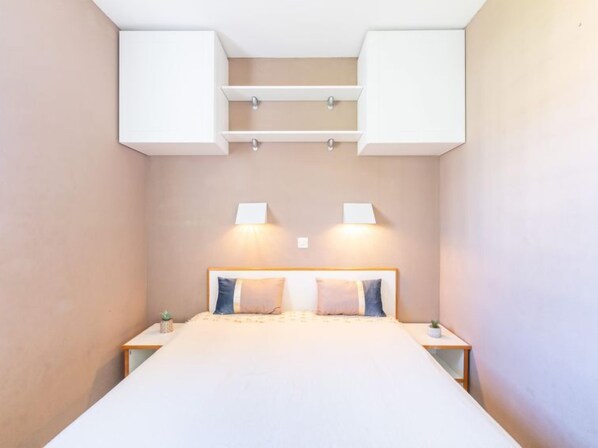 A bedroom with a bed, bedside tables, wall-mounted cabinets, and two wall-mounted lamps.