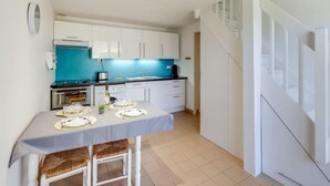 Een compacte keuken met witte kastjes, een blauwe achterwand en een eethoek voor vier personen.