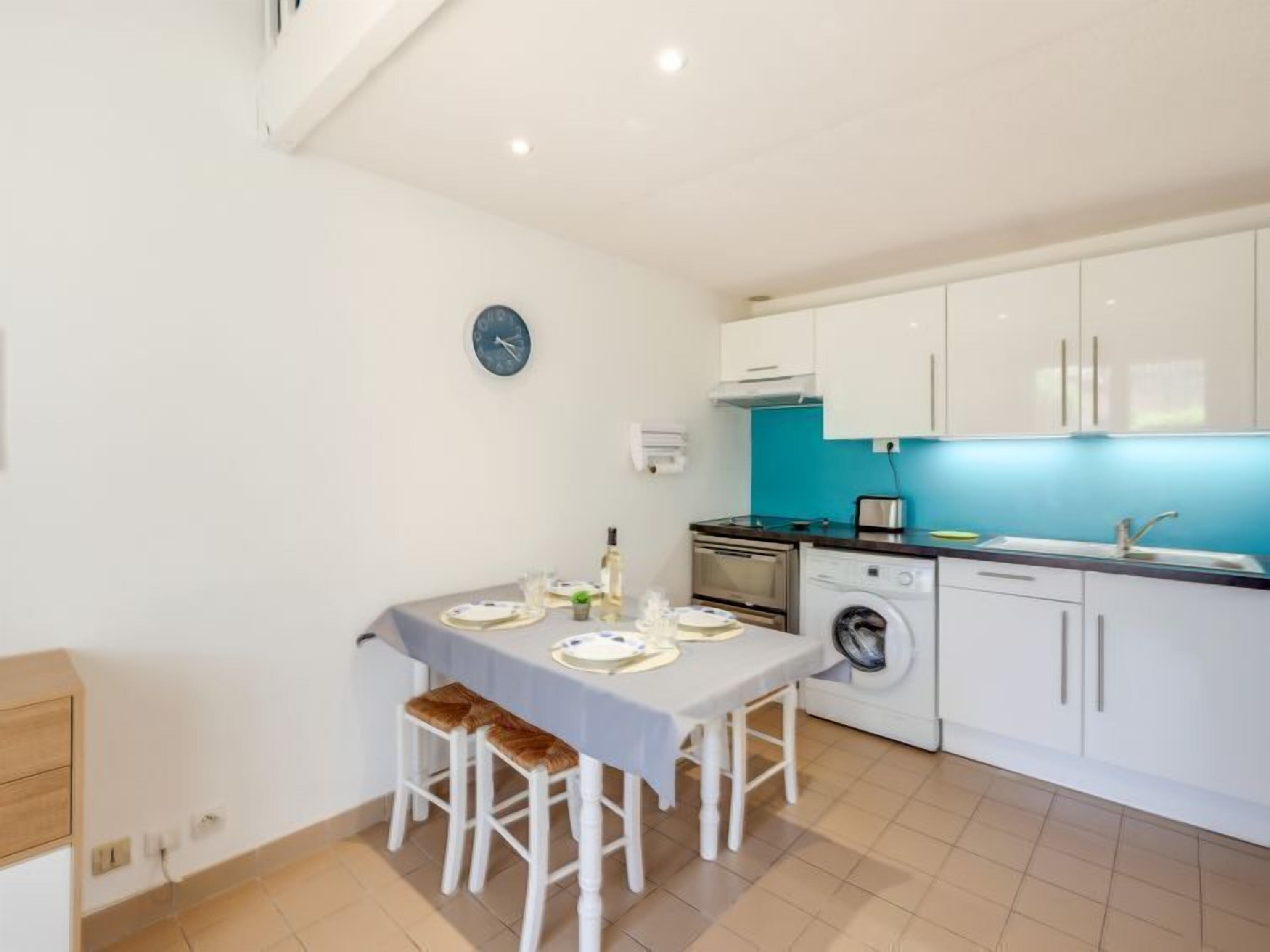 A compact kitchen with white cabinets, a washing machine, and a dining area with a table set for two.