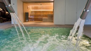 Moderni sisäuima-allas, jossa on kirkas vesi, ja sen ympärillä on pelkistetty sisustus sekä taustalla sijaitseva sauna.