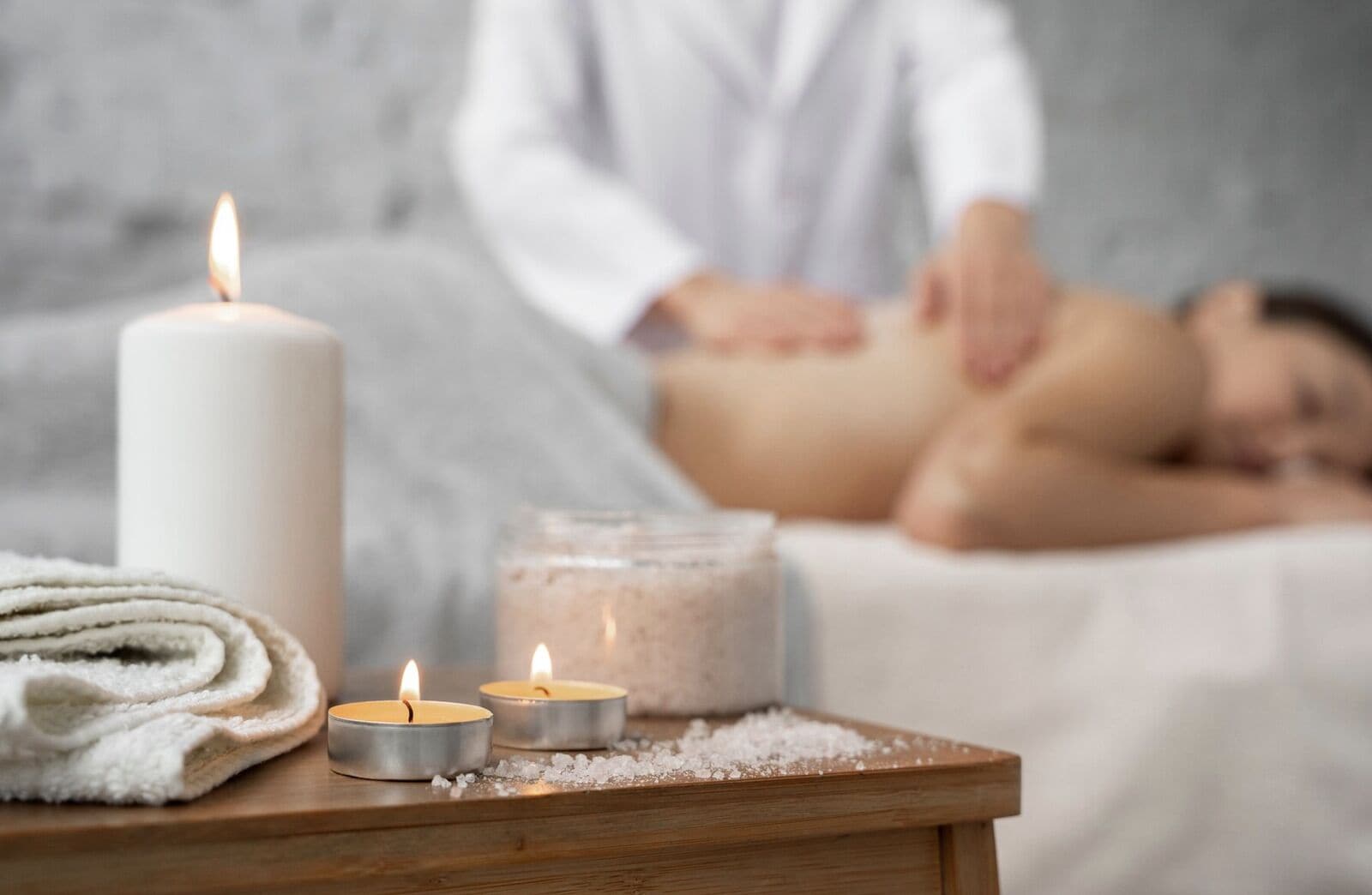 A spa setting with candles, a jar of salt, and a towel on a wooden table.