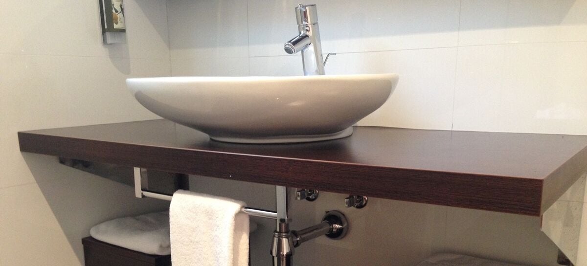 Un baño con un lavamanos blanco de diseño, un perchero y un inodoro, todo sobre un mostrador de madera oscura.
