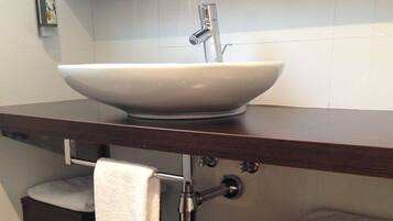 Un baño con un lavamanos blanco de diseño, un perchero y un inodoro, todo sobre un mostrador de madera oscura.