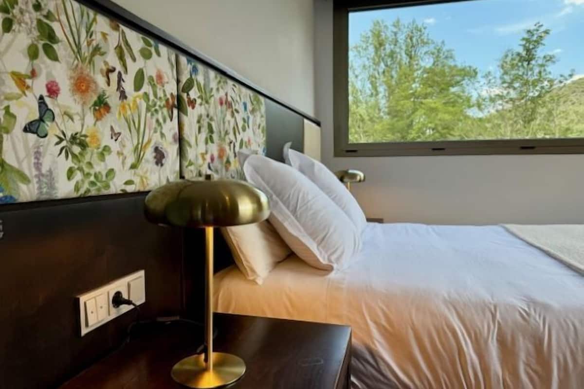 Een hotelkamer met een bed, nachtkastje, lamp en een hoofdbord met bloemenprint.