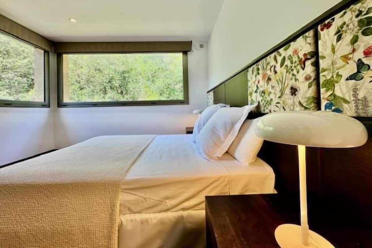 Een moderne slaapkamer met een groot raam, een bed met witte lakens en een hoofdeinde met een bloemmotief.