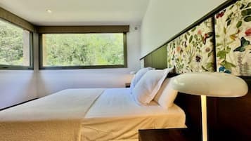Une chambre à coucher moderne avec une grande fenêtre, un lit recouvert de draps blancs et une tête de lit à motifs floraux.