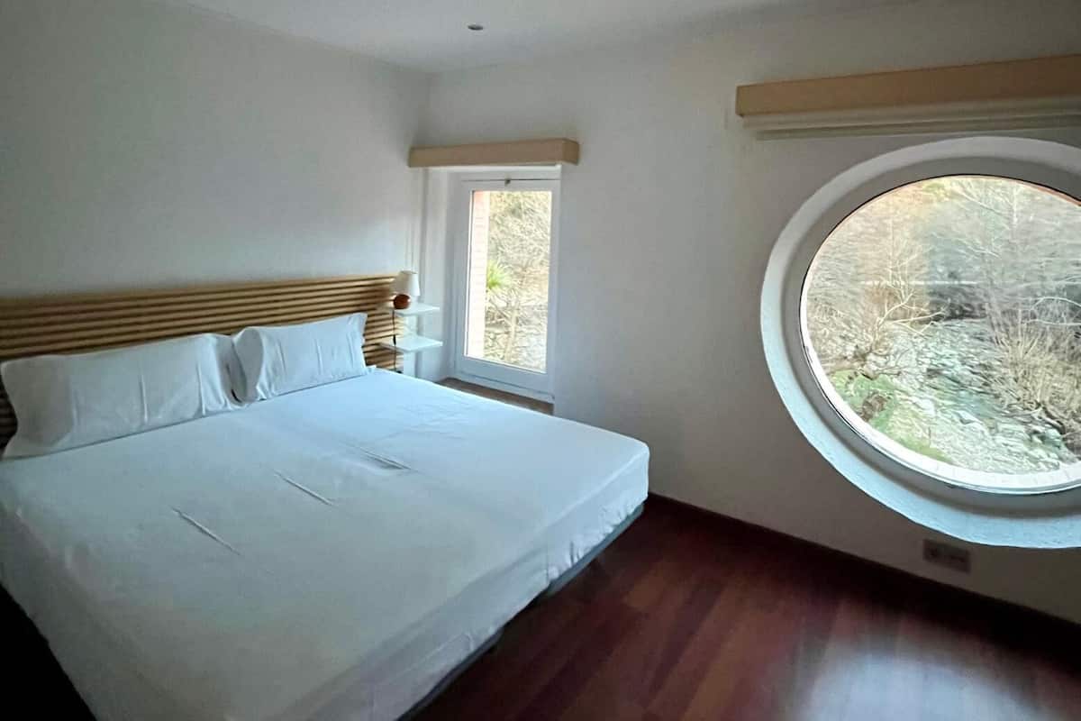 Een slaapkamer met een groot bed, een raam en een rond dakvenster.