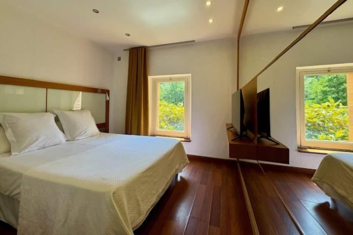 Een moderne hotelkamer met een groot bed, een flatscreen televisie en twee ramen met uitzicht op groen.