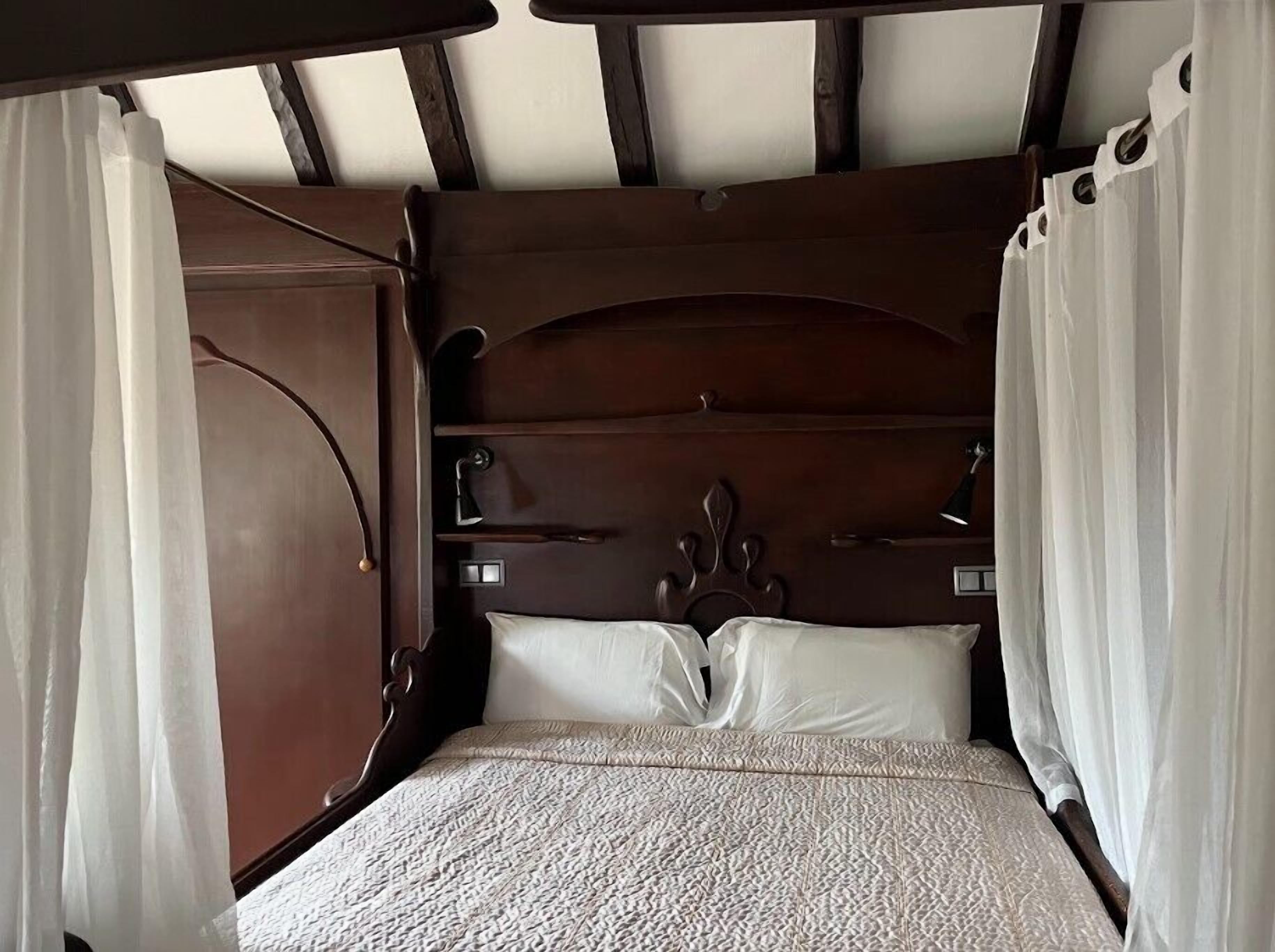 Una cama de madera con cabecera, cortinas blancas y una colcha con textura.
