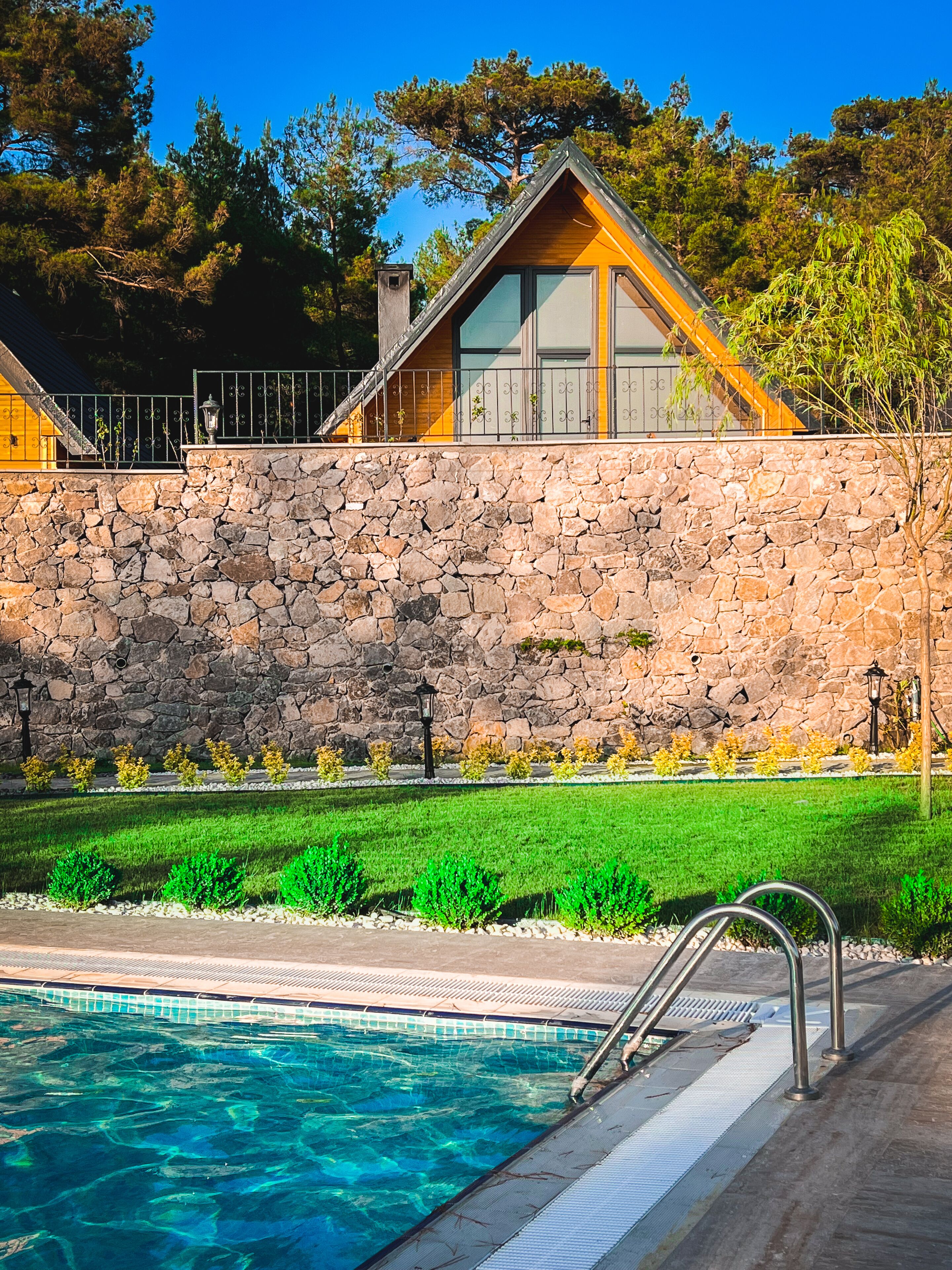 A modern house with a stone wall, a swimming pool, and a well-maintained garden.