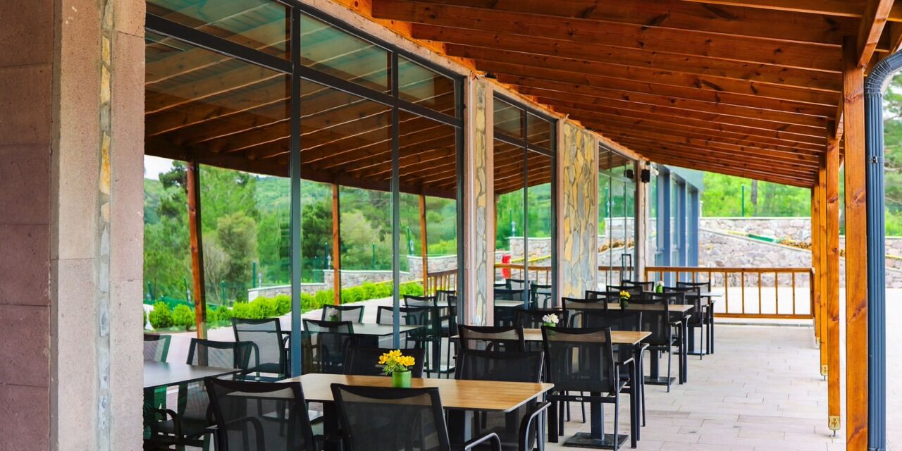 Ein Straßencafé mit Tischen, Stühlen, großen Fenstern und einer Holzzieldecke.