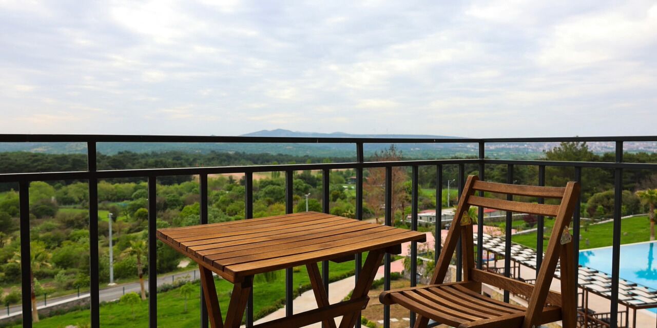 Un balcón con una mesa y una silla de madera, con vista a una piscina y follaje.