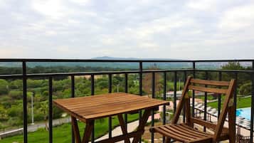 Un balcón con una mesa y una silla de madera, con vista a una piscina y follaje.