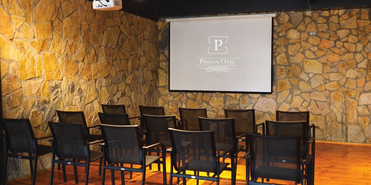 Une salle de conférence aux murs en pierre, dotée d’un écran de projection et de rangées de chaises.