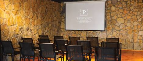 Une salle de conférence aux murs en pierre, dotée d’un écran de projection et de rangées de chaises.
