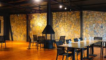 Un salón de conferencias con pared de piedra, chimenea negra, mesas y sillas de madera.