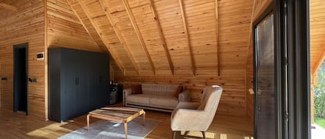 A wooden interior with a high ceiling, a sofa, a chair, a small table, and a cabinet.