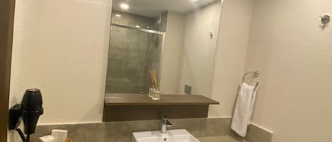 A modern bathroom with a white sink, a mirror above it, and a shower visible in the reflection.
