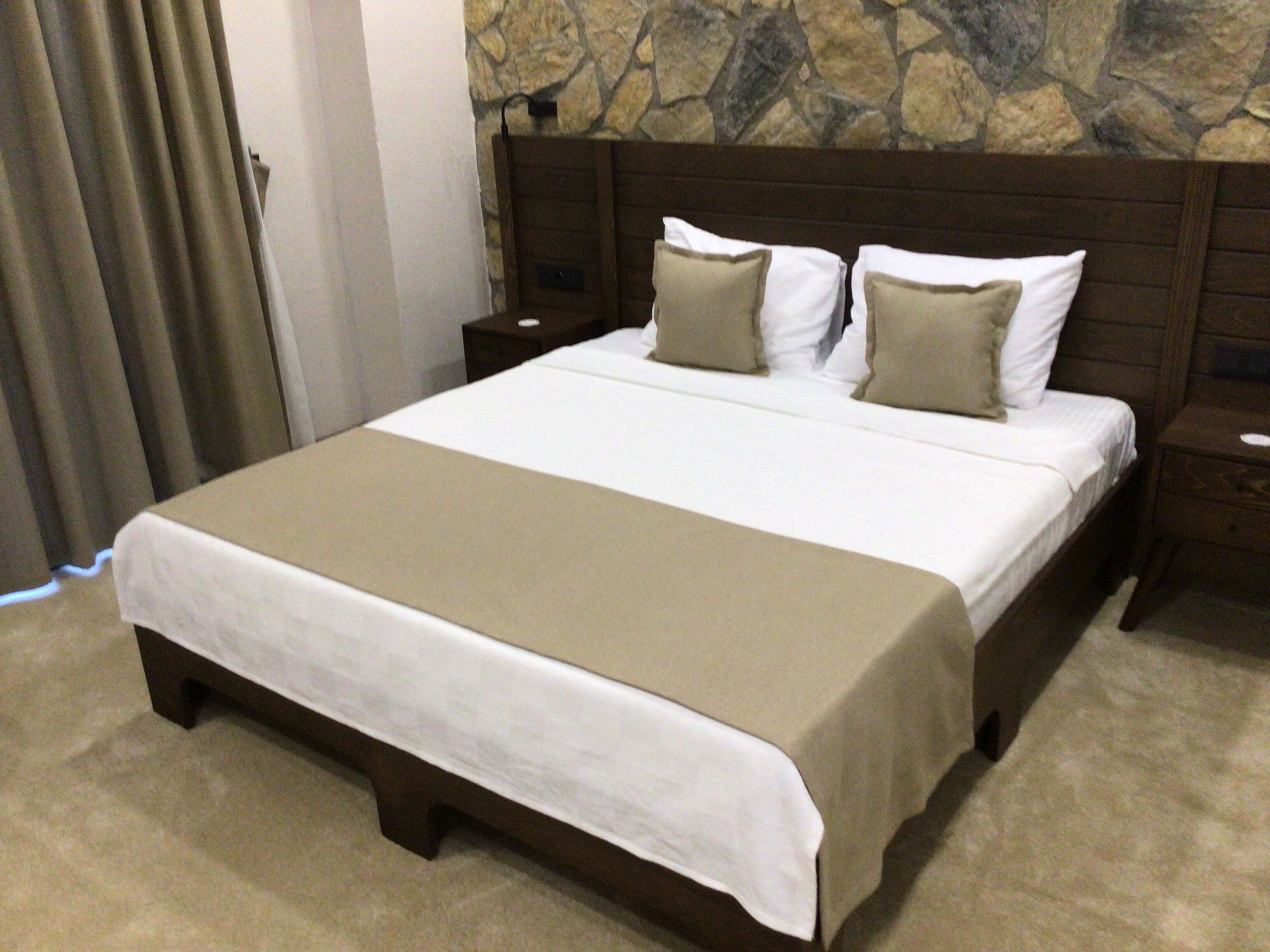 A hotel room with a large bed, a stone wall, and a wooden headboard.