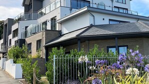 A modern two-story residential building with a balcony, a garage, and a well-maintained garden with flowers.