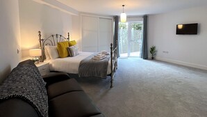 A bedroom with a bed, bedside table, lamp, and a TV on the wall.