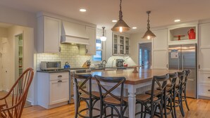 A spacious kitchen with a central island, bar stools, and modern appliances. - Little Grey Cottage - Beautifully decorated large vacation home - Walking distance to Lake Michigan! (Douglas)