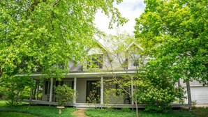 A two-story house with a porch, surrounded by lush greenery and trees. - Little Grey Cottage - Beautifully decorated large vacation home - Walking distance to Lake Michigan! (Douglas)