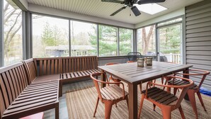 A covered patio with a wooden table and chairs, a bench, and a ceiling fan. - Little Grey Cottage - Beautifully decorated large vacation home - Walking distance to Lake Michigan! (Douglas)
