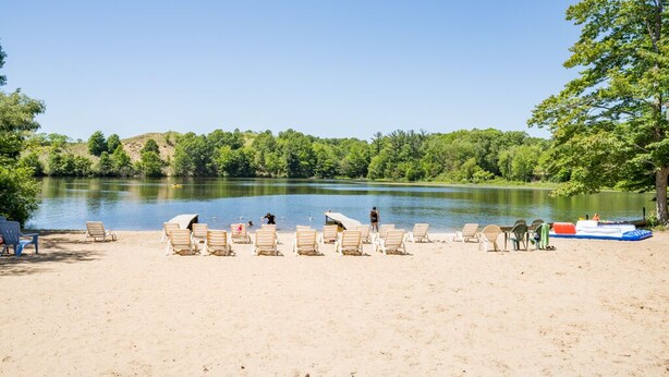 A lakeside beach with rows of beach chairs and a boat on the water.