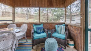 A covered porch with wicker furniture, a striped rug, and a view of the backyard.