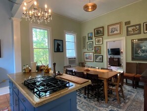 A kitchen with a gas stove, wooden cabinets, a chandelier, and a dining area with a table and chairs.