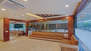 A spacious lobby with a large sofa, a reception desk, and a large window offering a view of the outdoors. - Hotel Taj Venture By Park Tree (Agra)