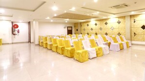 A spacious hall with rows of chairs covered in yellow and white, a fire extinguisher, and a ceiling fan. - Hotel Taj Venture By Park Tree (Agra)