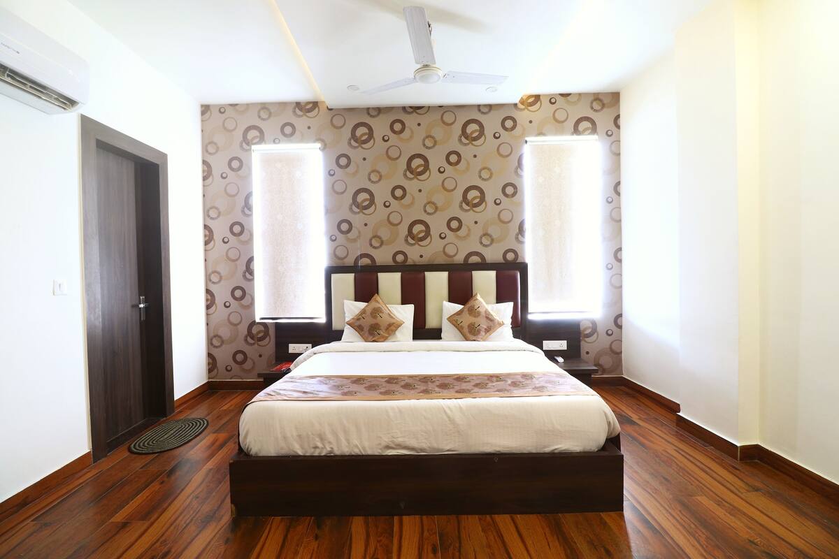 Quarto com piso de madeira, cama com cabeceira, duas mesas de cabeceira e um ventilador de teto.
