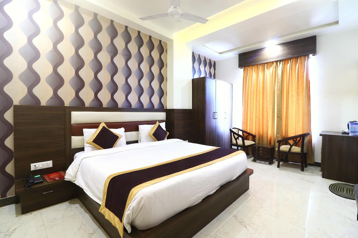 Quarto de hotel com cama grande, escrivaninha, duas cadeiras, guarda-roupa e ventoinha no teto.