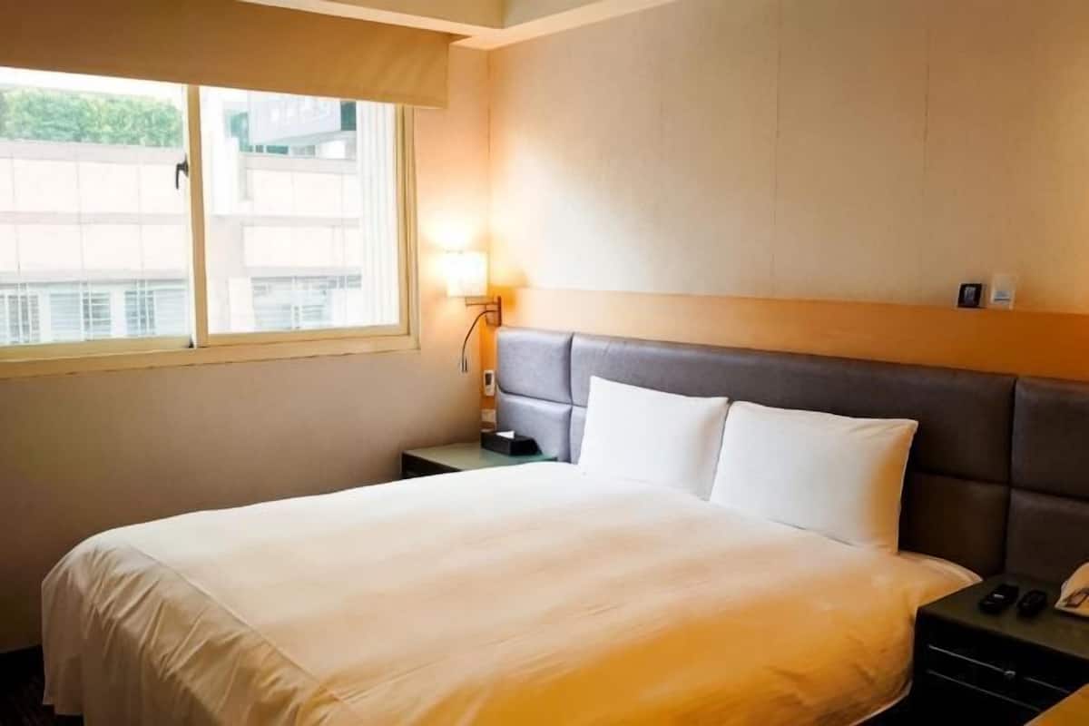 Une chambre d’hôtel avec un lit, une table de chevet, une lampe et une fenêtre.