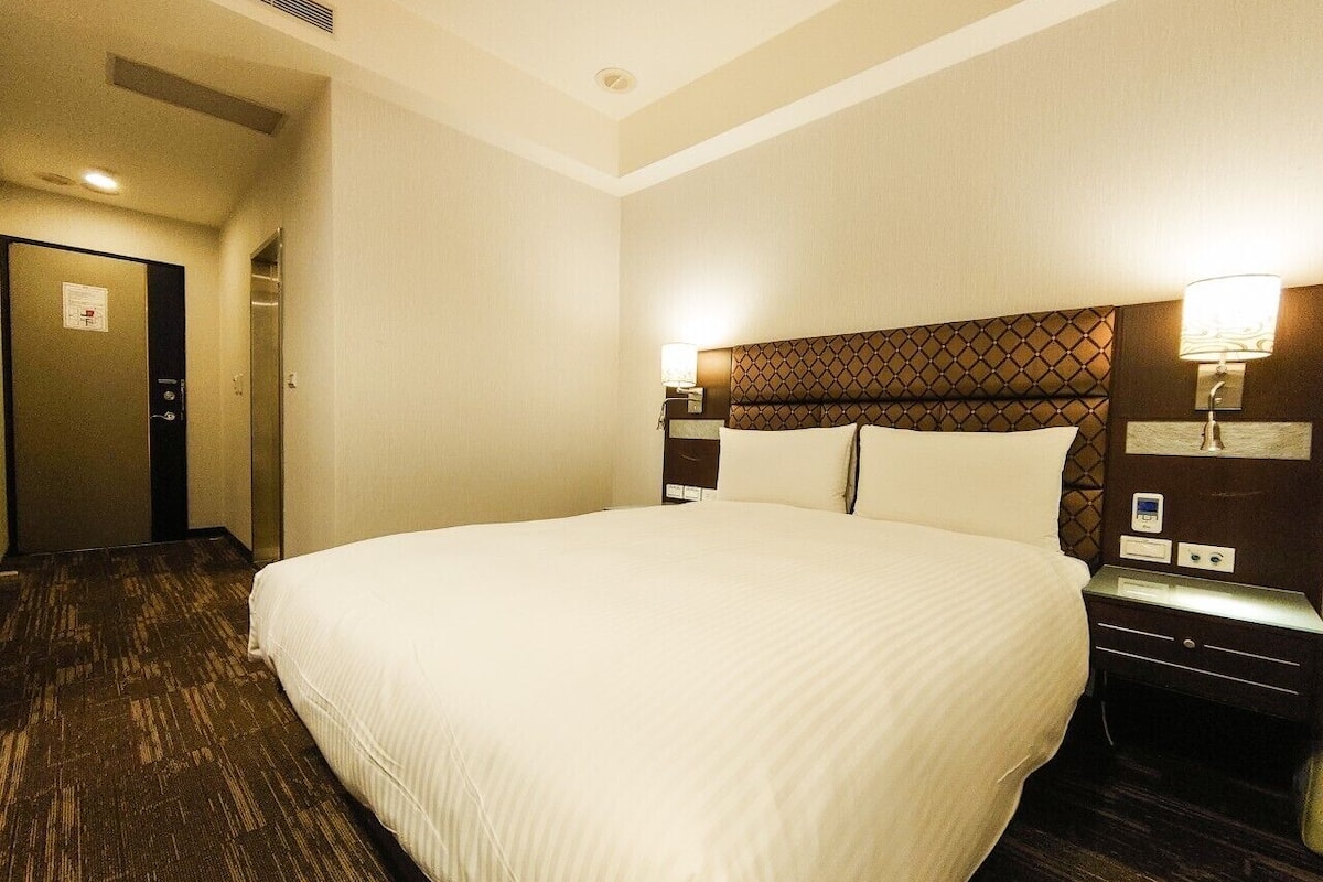 Une chambre d’hôtel avec un grand lit, une tête de lit ornée d’un motif géométrique, des lampes de chevet et un sol recouvert de moquette.