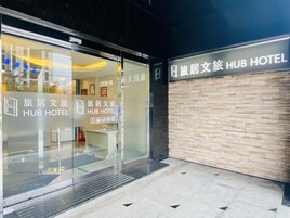 Exterior de un hotel con fachada de vidrio y señalización que indica que es un 'Hub Hotel'.