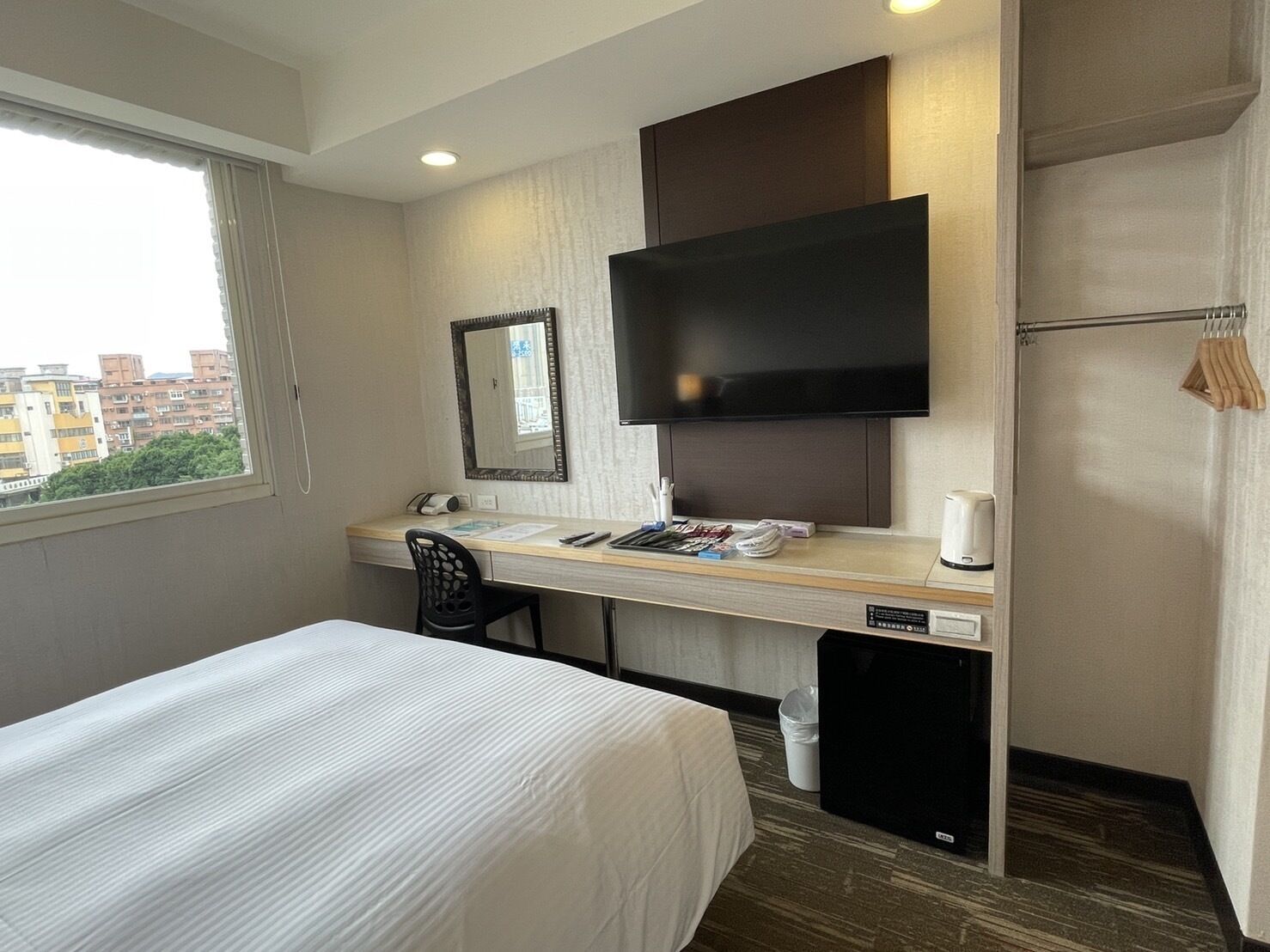 A hotel room with a bed, a desk with a chair, a TV, and a window.