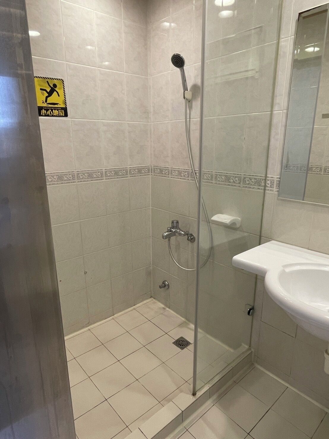 A bathroom with a glass shower enclosure, a white sink, and a tiled floor.