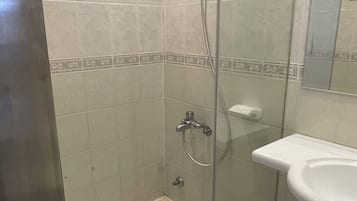 A bathroom with a glass shower enclosure, a white sink, and a tiled floor.