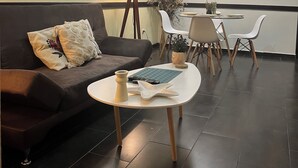 A modern living room with a dark brown sofa, a small white table, and a dining area with chairs and a lamp.