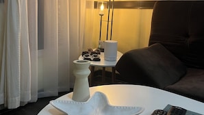 A hotel room with a round white table, a white vase, and a remote control on a blue mat.