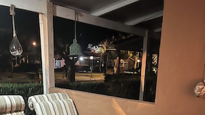 A patio area with striped sofas and a glass-top table, overlooking a well-lit outdoor space with trees and a building in the background.