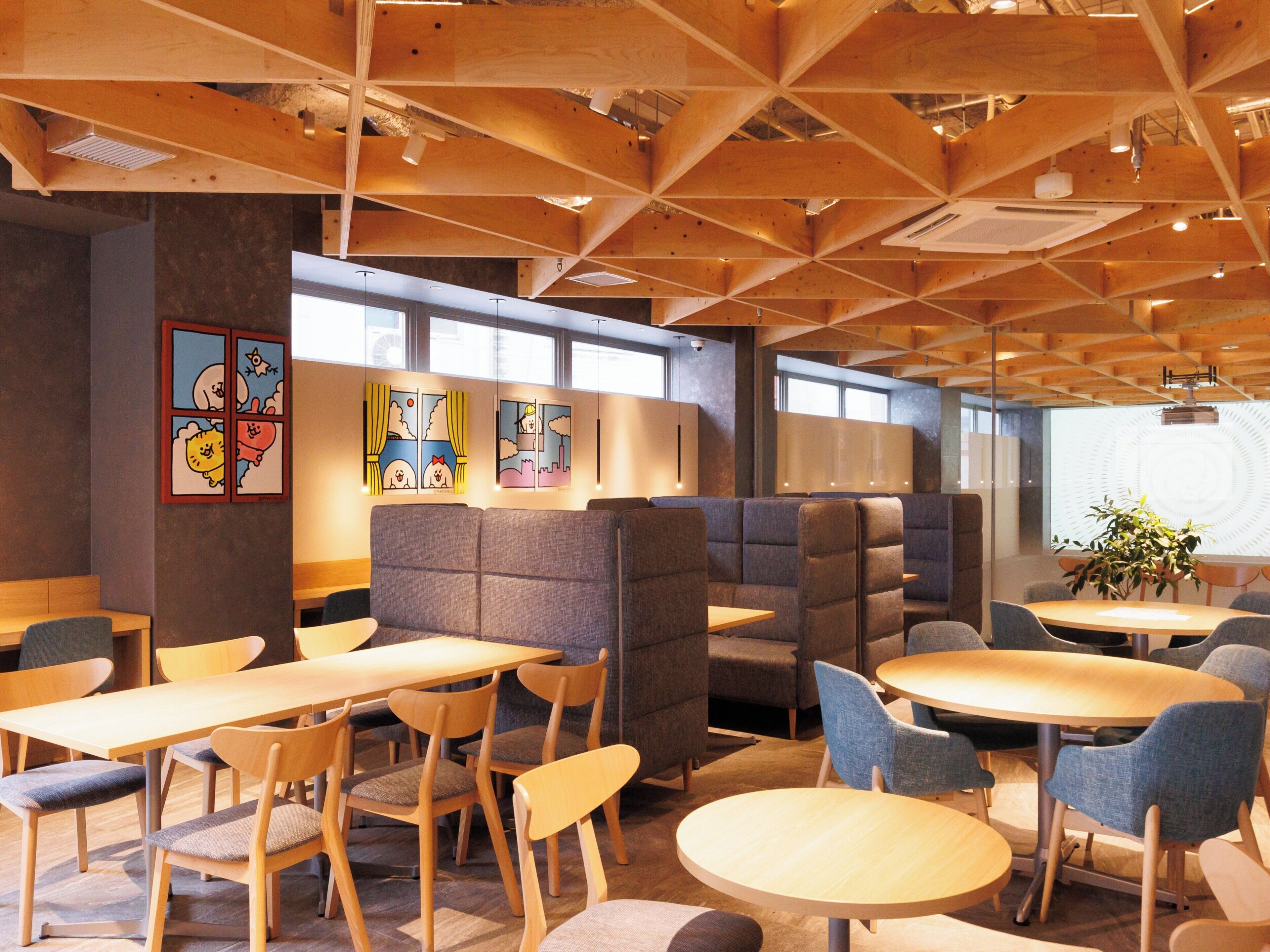 A modern restaurant interior with wooden ceiling beams, cushioned booths, and round tables.